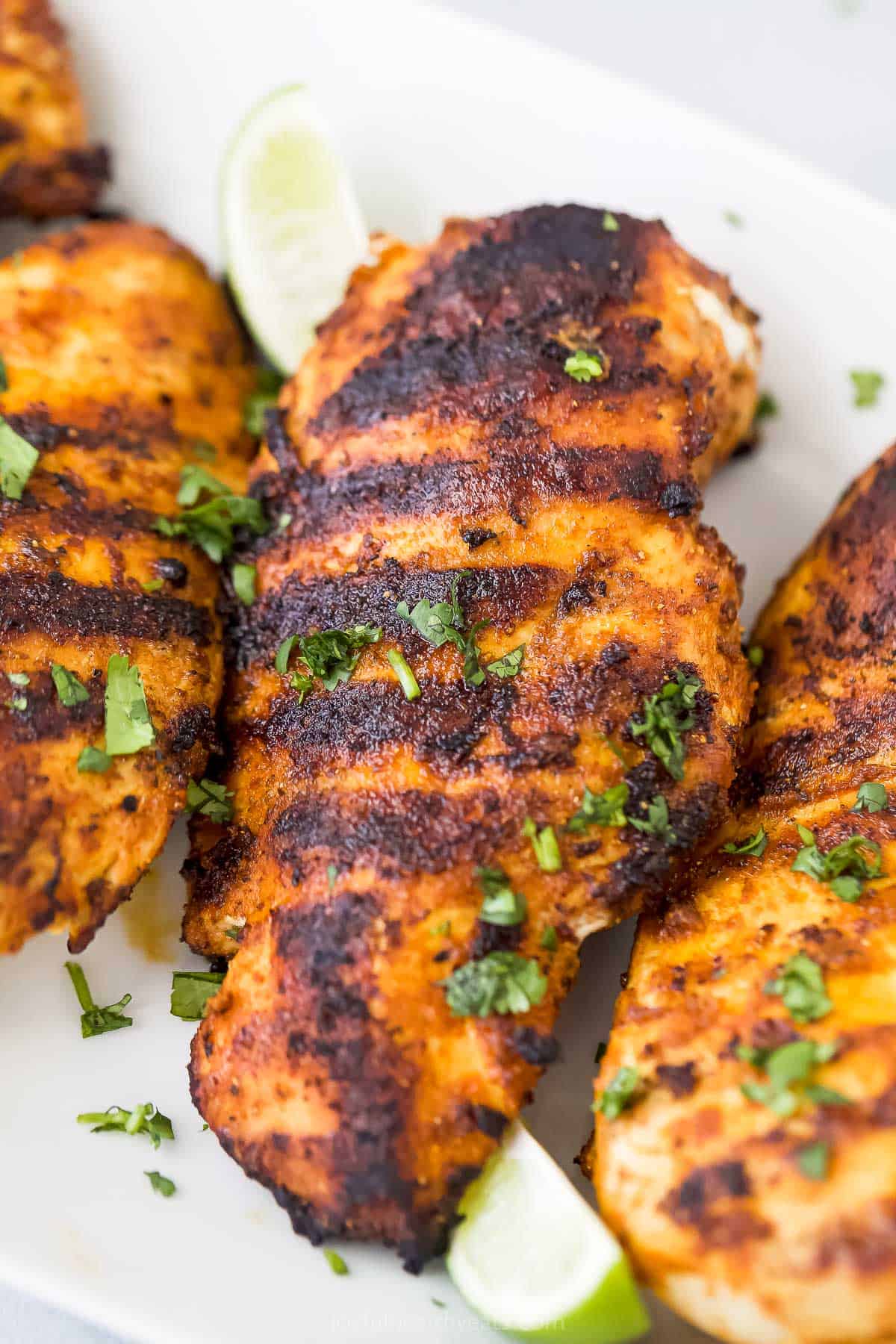 A close-up shot of a grilled chicken breast on a platter with three other breasts