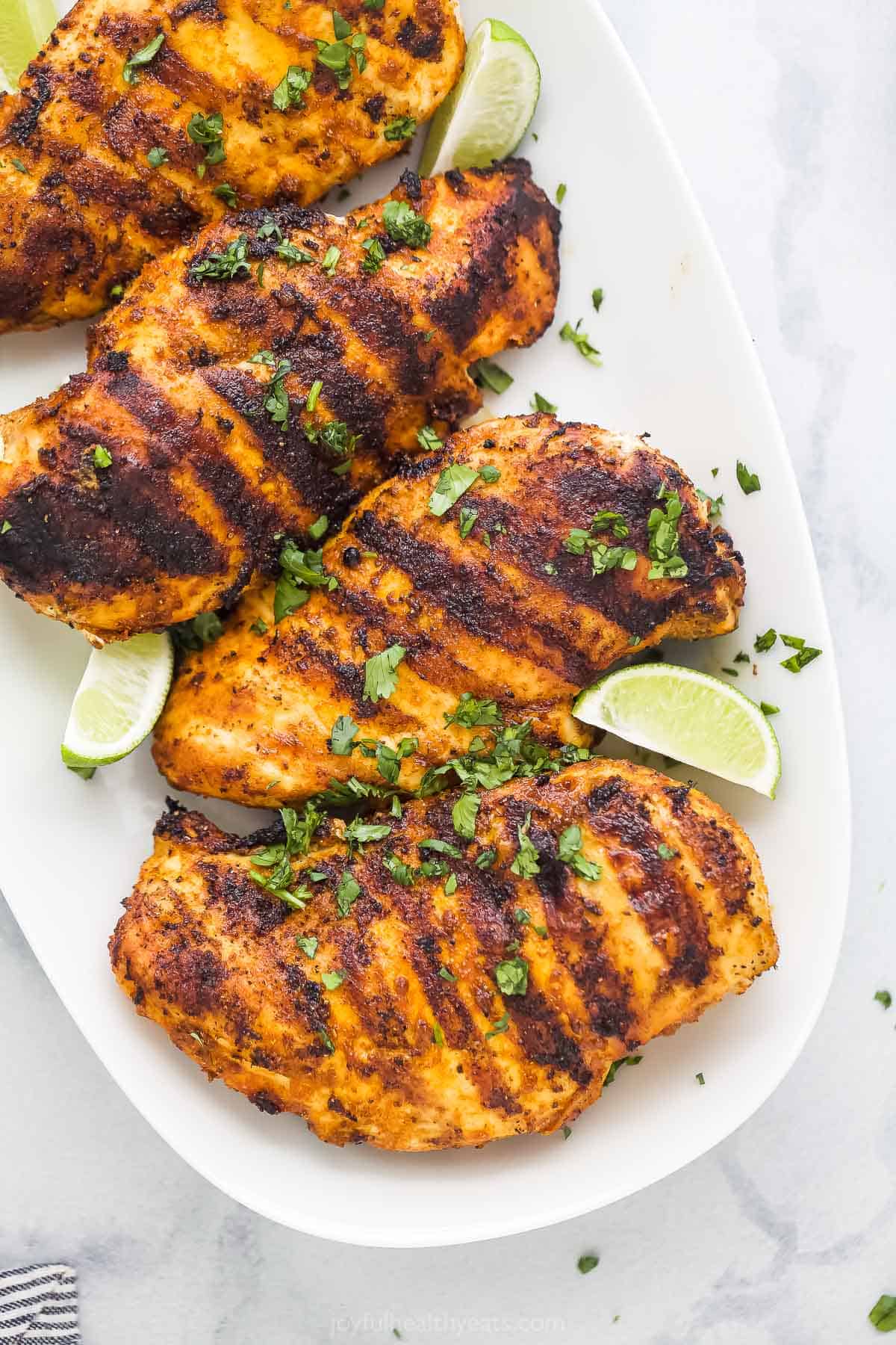 Four grilled chicken breasts on a white serving platter with lime wedges