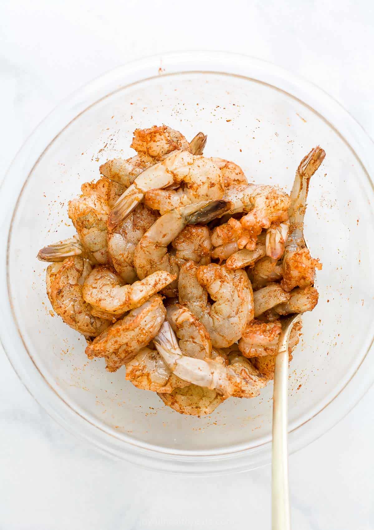 Seasoned shrimp inside of a glass mixing bowl on a countertop