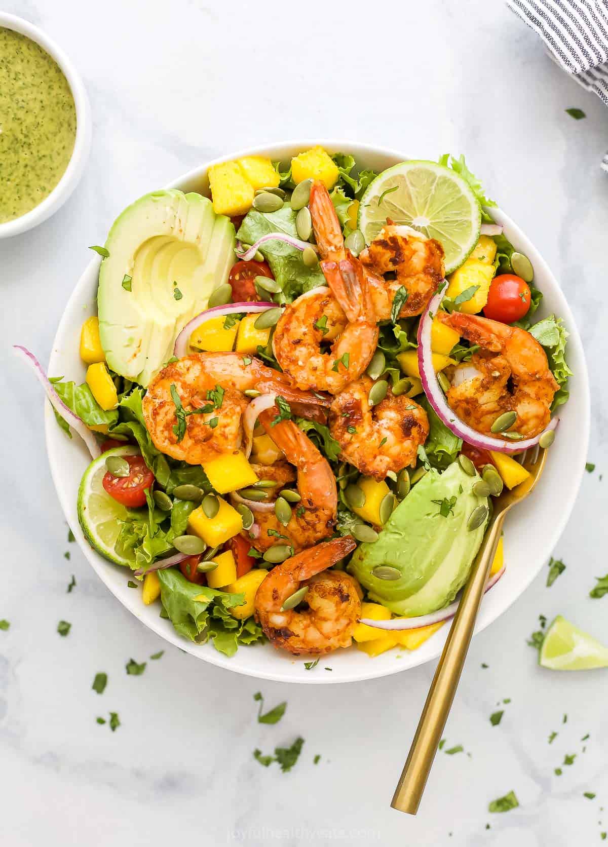 A bowl of shrimp avocado salad beside a smaller bowl filled with cilantro lime dressing