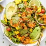 A mango avocado shrimp salad in a bowl with a golden spoon inside