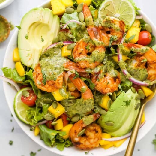 A mango avocado shrimp salad in a bowl with a golden spoon inside