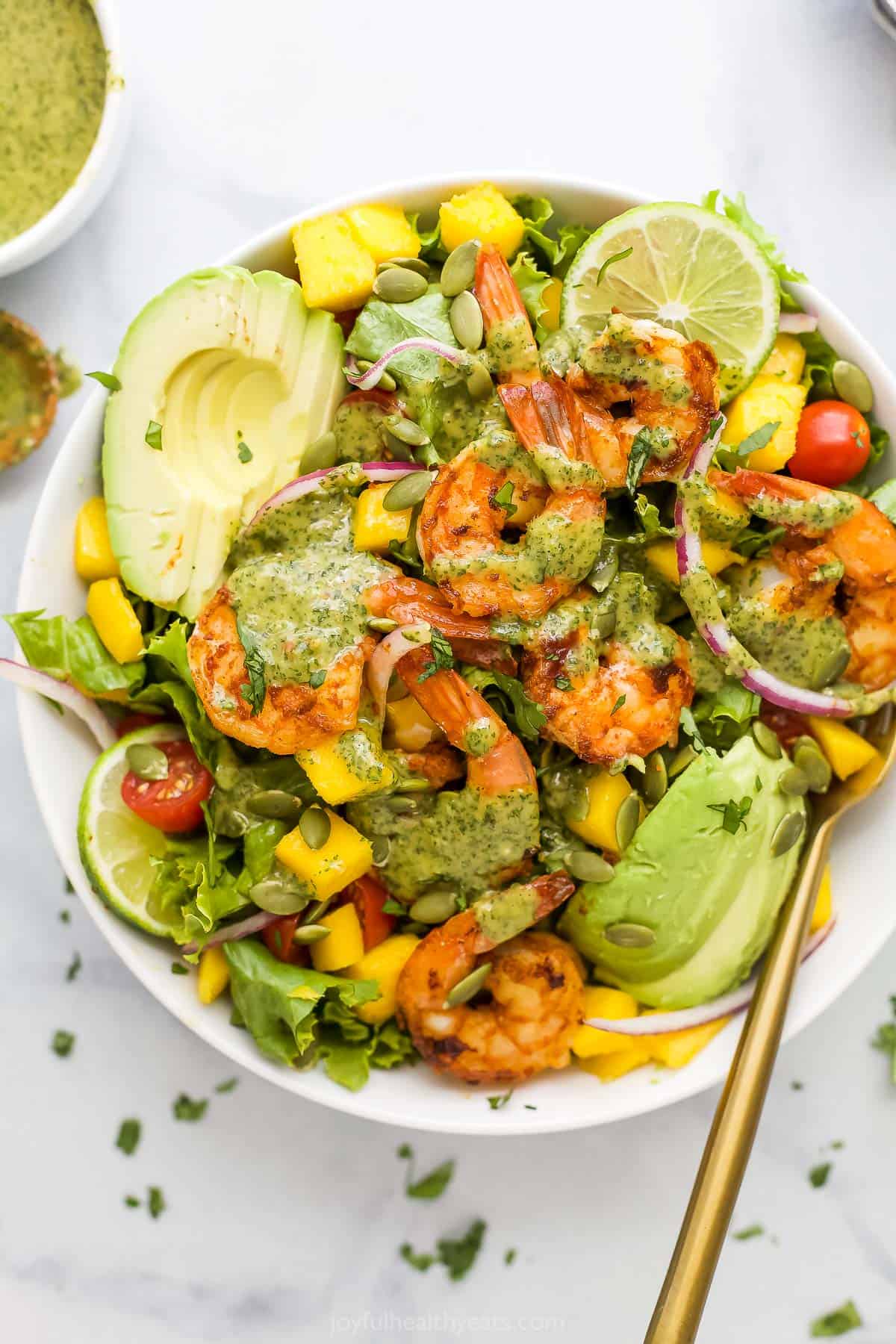 A mango avocado shrimp salad in a bowl with a golden spoon inside