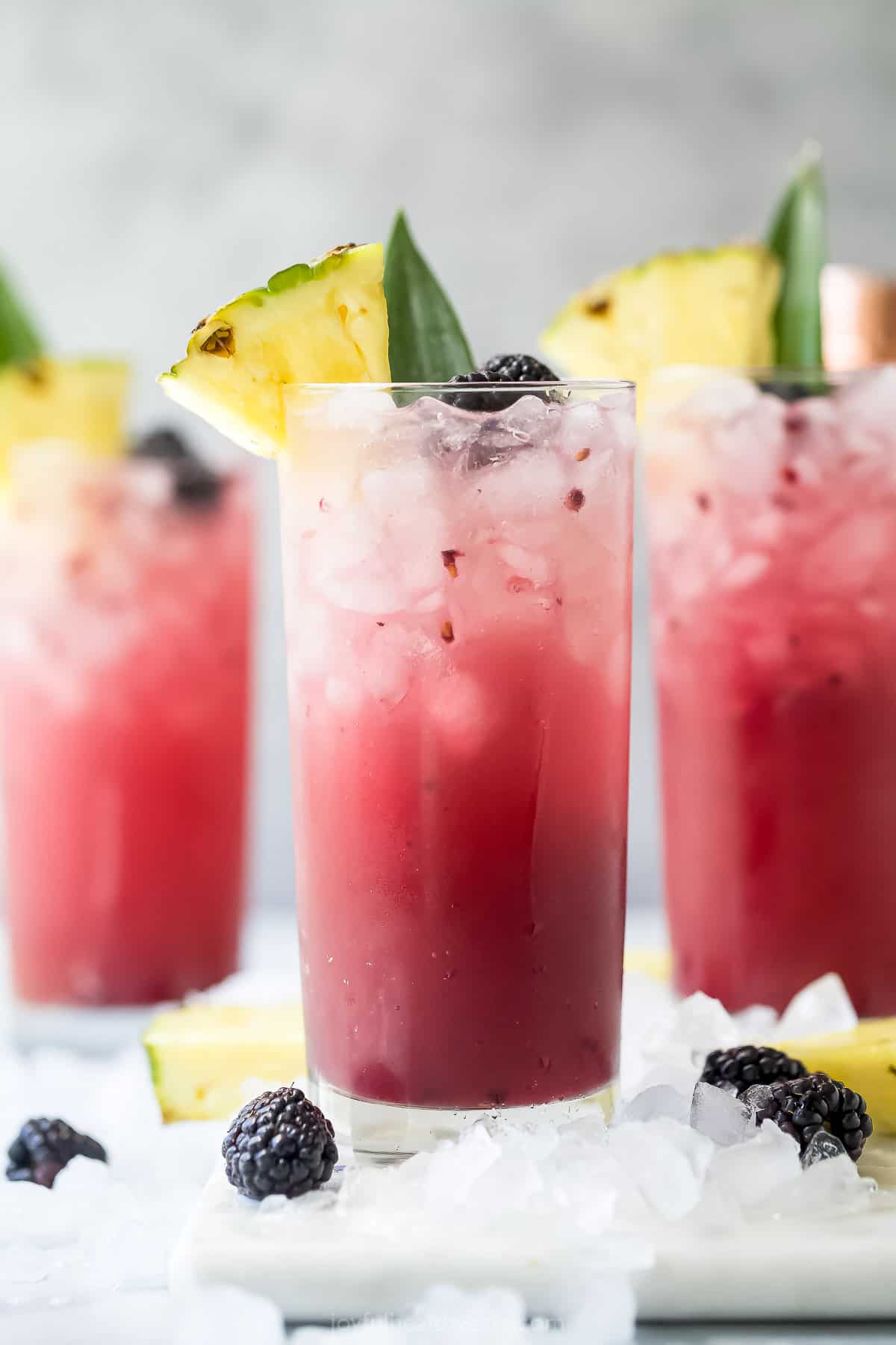 A close-up shot of three virgin pineapple cocktails garnished with pineapple wedges and raspberries