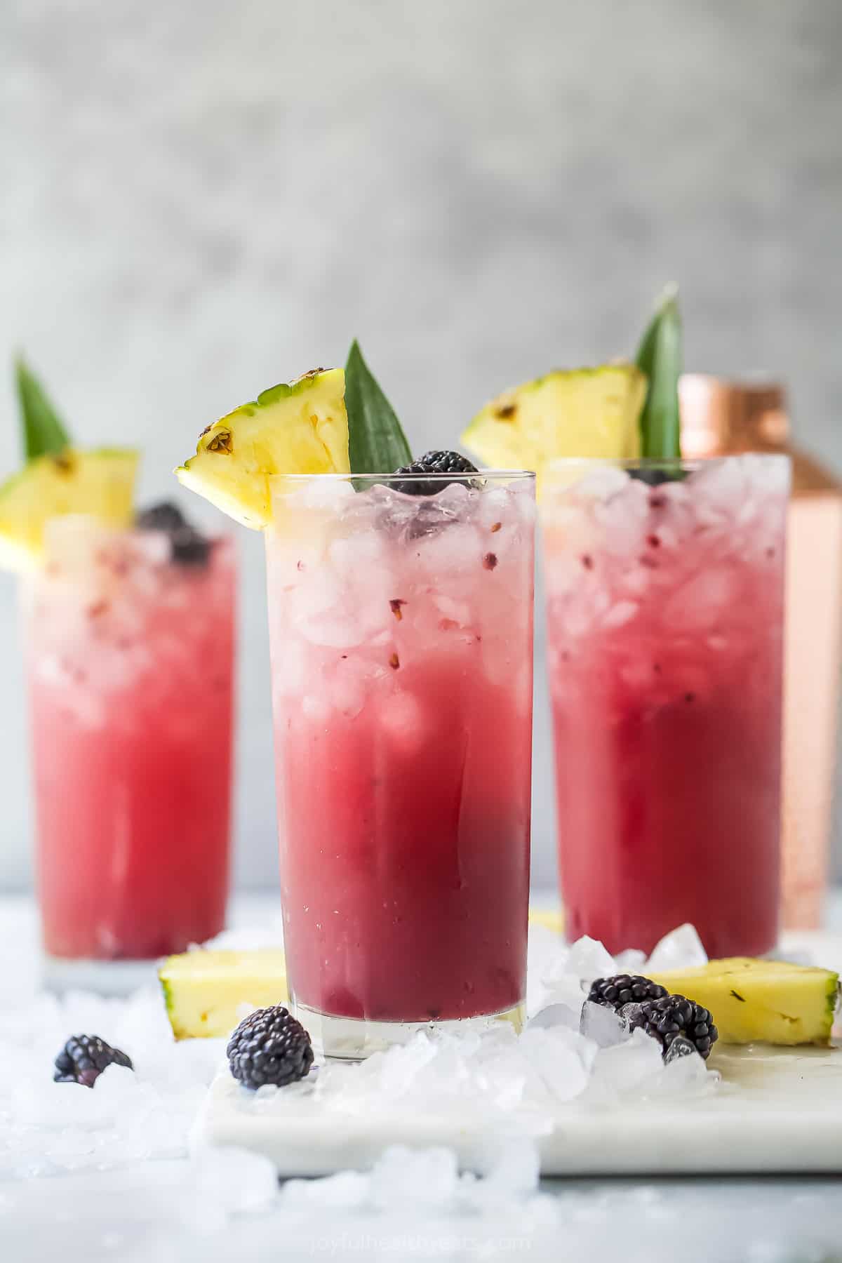 Three virgin mixed drinks on a kitchen countertop with a cocktail shaker behind them