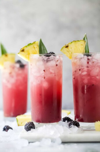 Two pineapple ginger beer mocktails on a cutting board with a third mocktail in the background