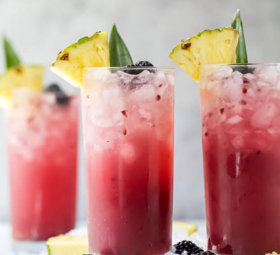 Two pineapple ginger beer mocktails on a cutting board with a third mocktail in the background