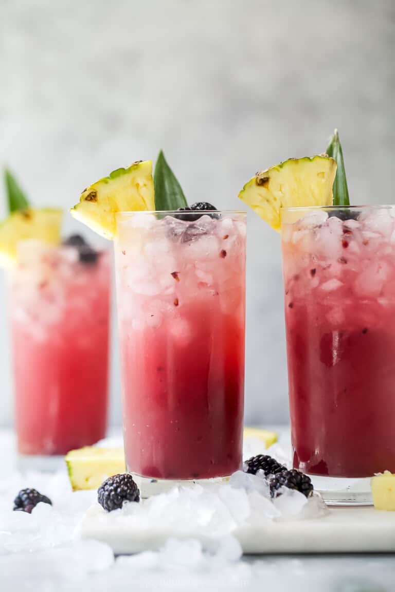 a high ball glass with pink beverage, ice, and pineapple garnish