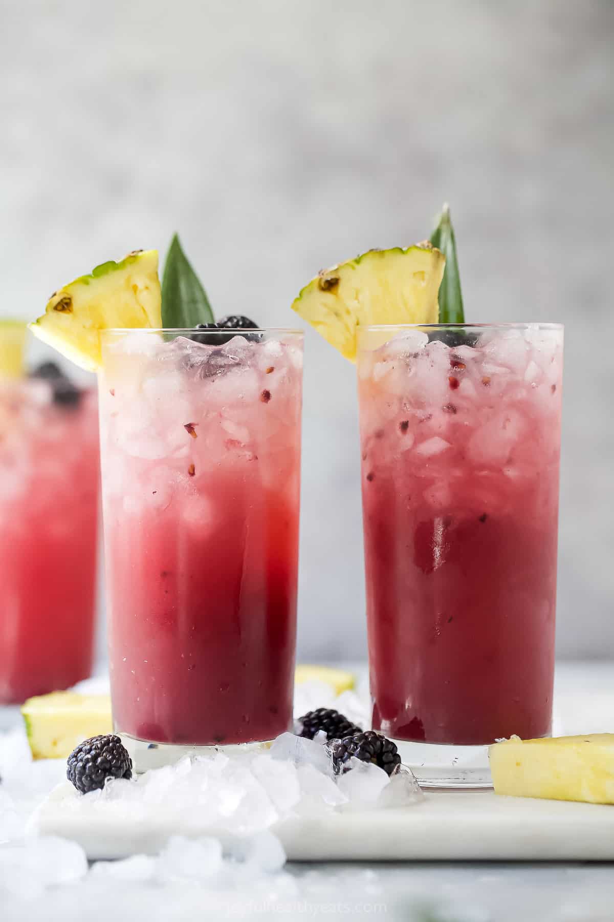 Three virgin blackberry pineapple cocktails in tall glasses with crushed ice inside