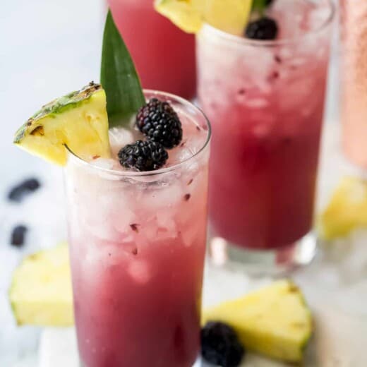 Three pineapple ginger beer mocktails on a cutting board with fresh blackberries and pineapple slices