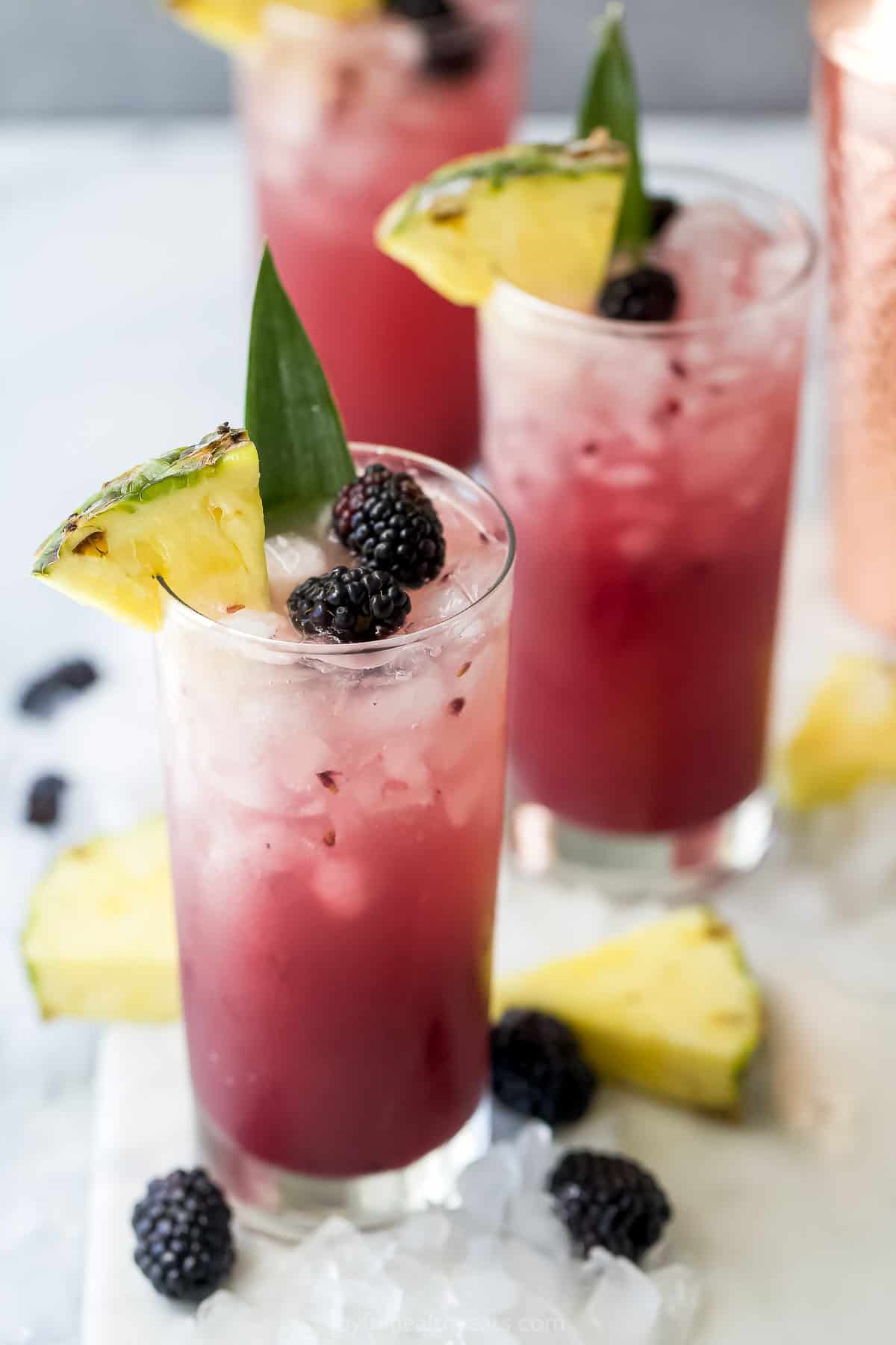 Three pineapple ginger beer mocktails on a cutting board with fresh blackberries and pineapple slices