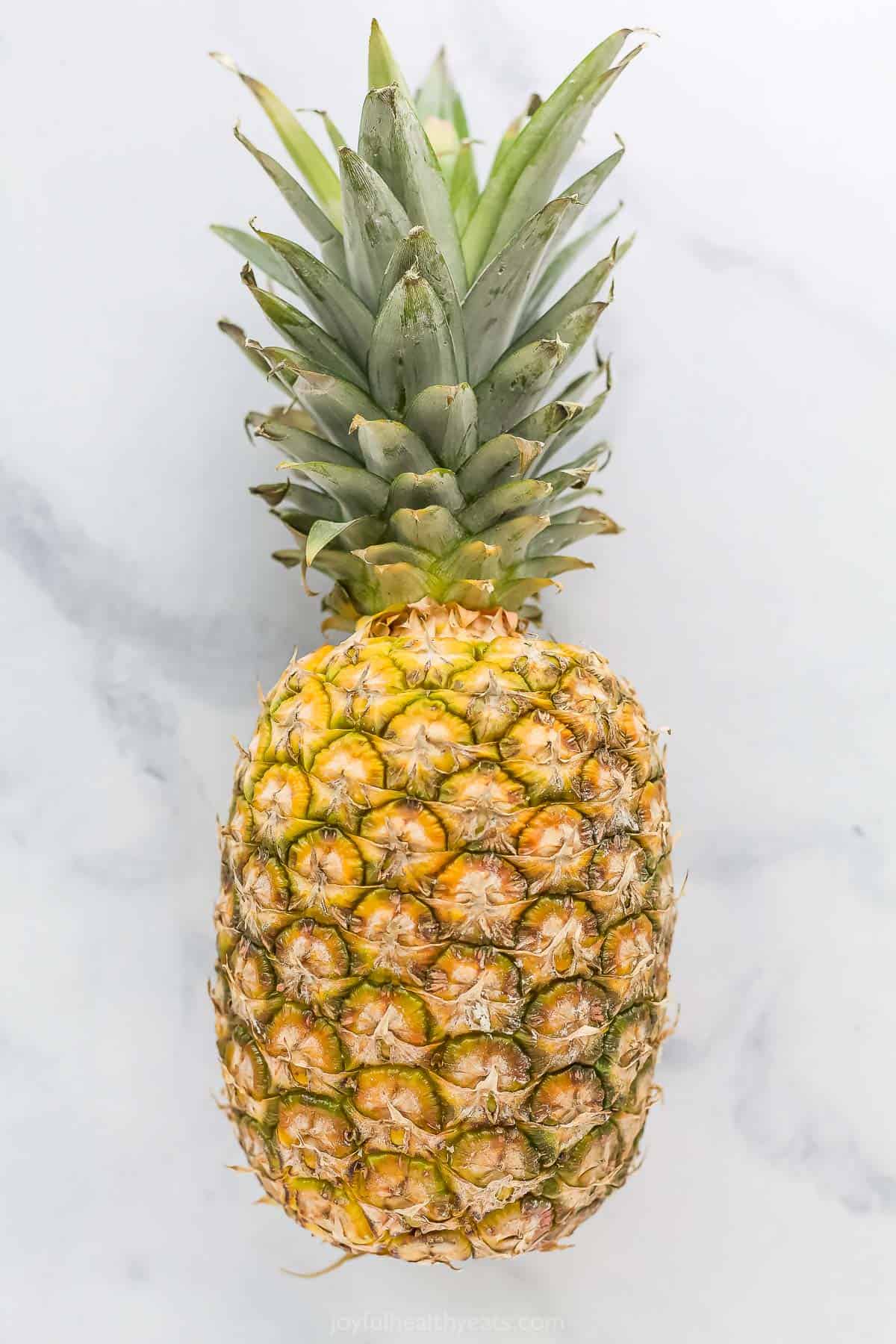 A fresh pineapple laying down on a gray and white marble countertop