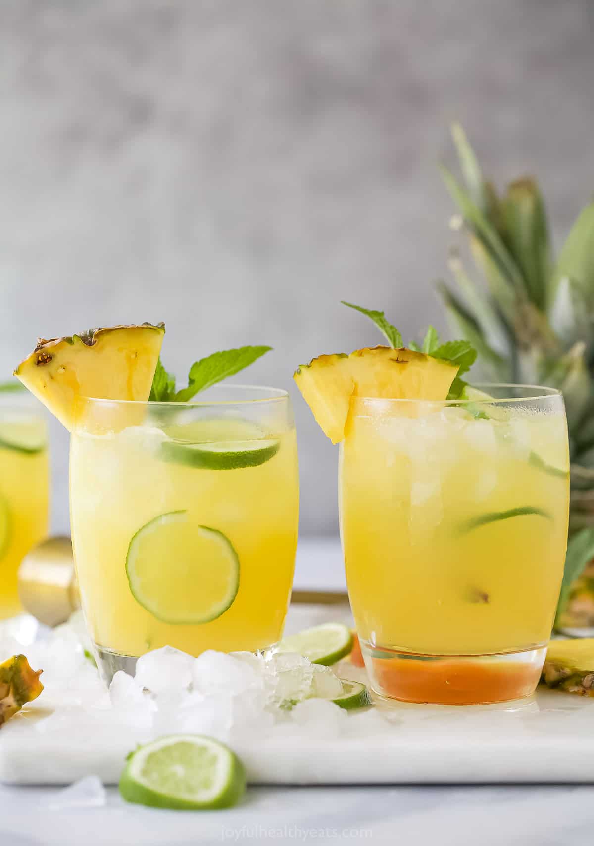 Two pineapple rum punches on a plastic cutting board