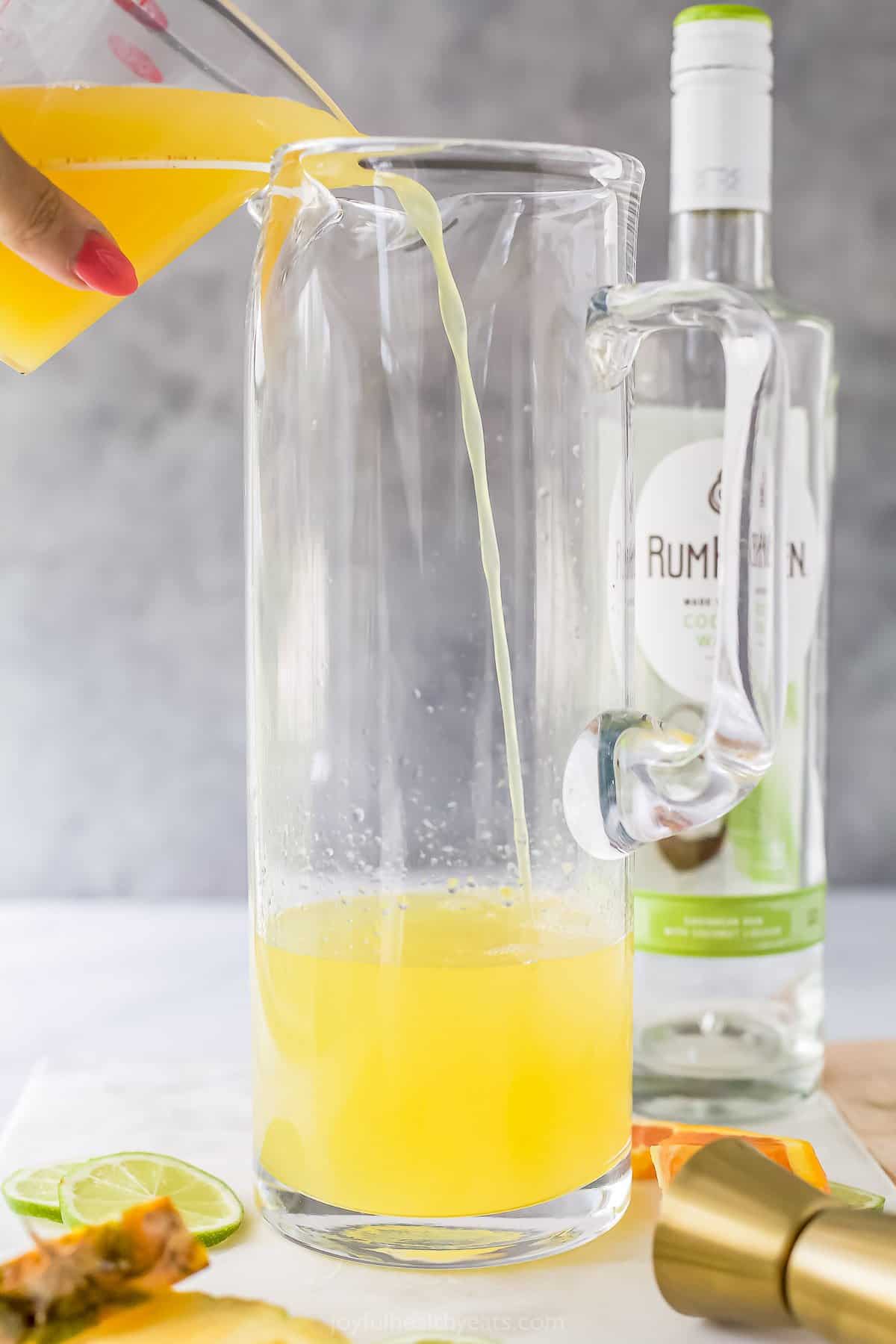 The pineapple juice mixture being poured into a tall pitcher