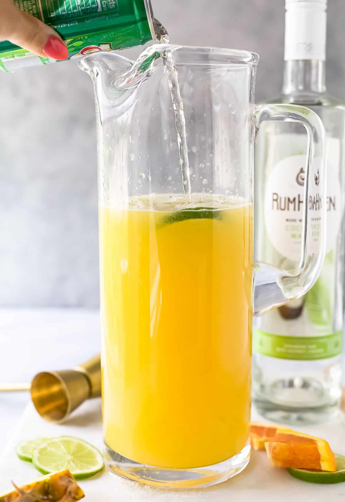 A can of ginger ale being poured into a pitcher containing rum punch