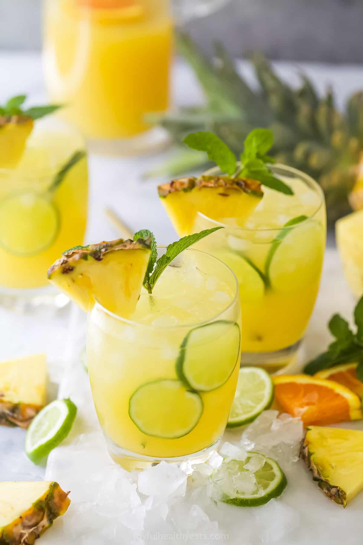 A bunch of pineapple cocktails on a countertop with a large pineapple behind them