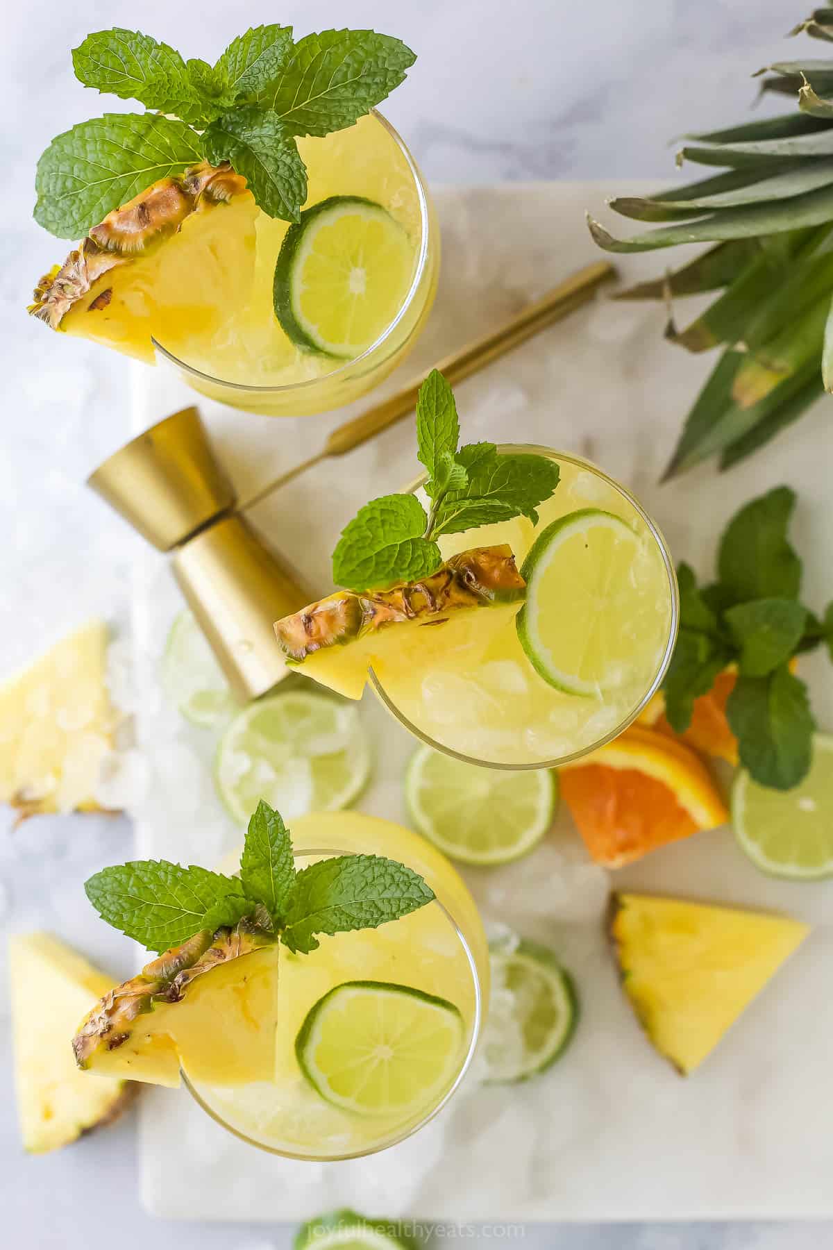 Three glasses of pineapple rum punch garnished with mint leaves and fresh fruit slices