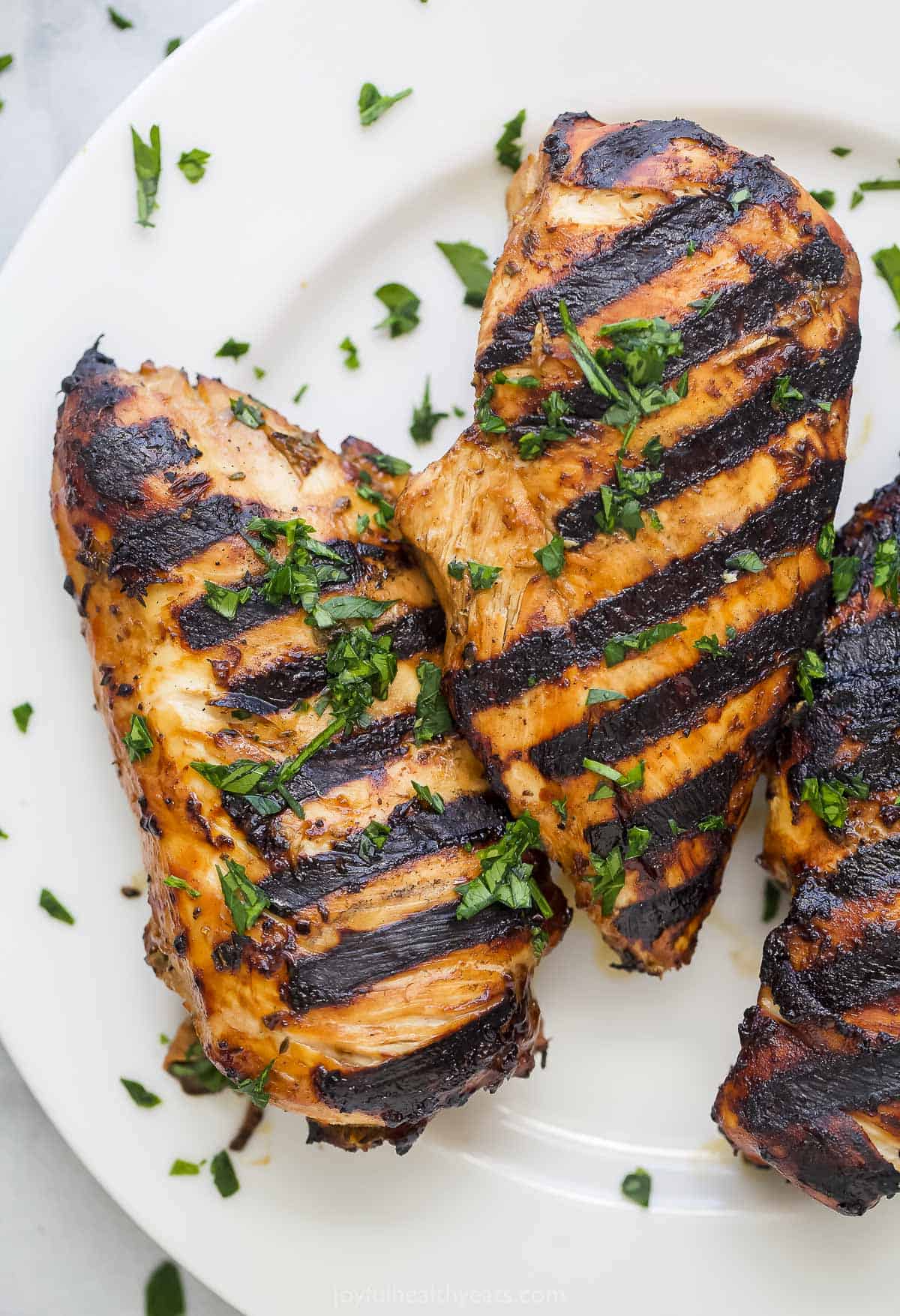 Three balsamic grilled chicken breasts on a white plate with a raised rim
