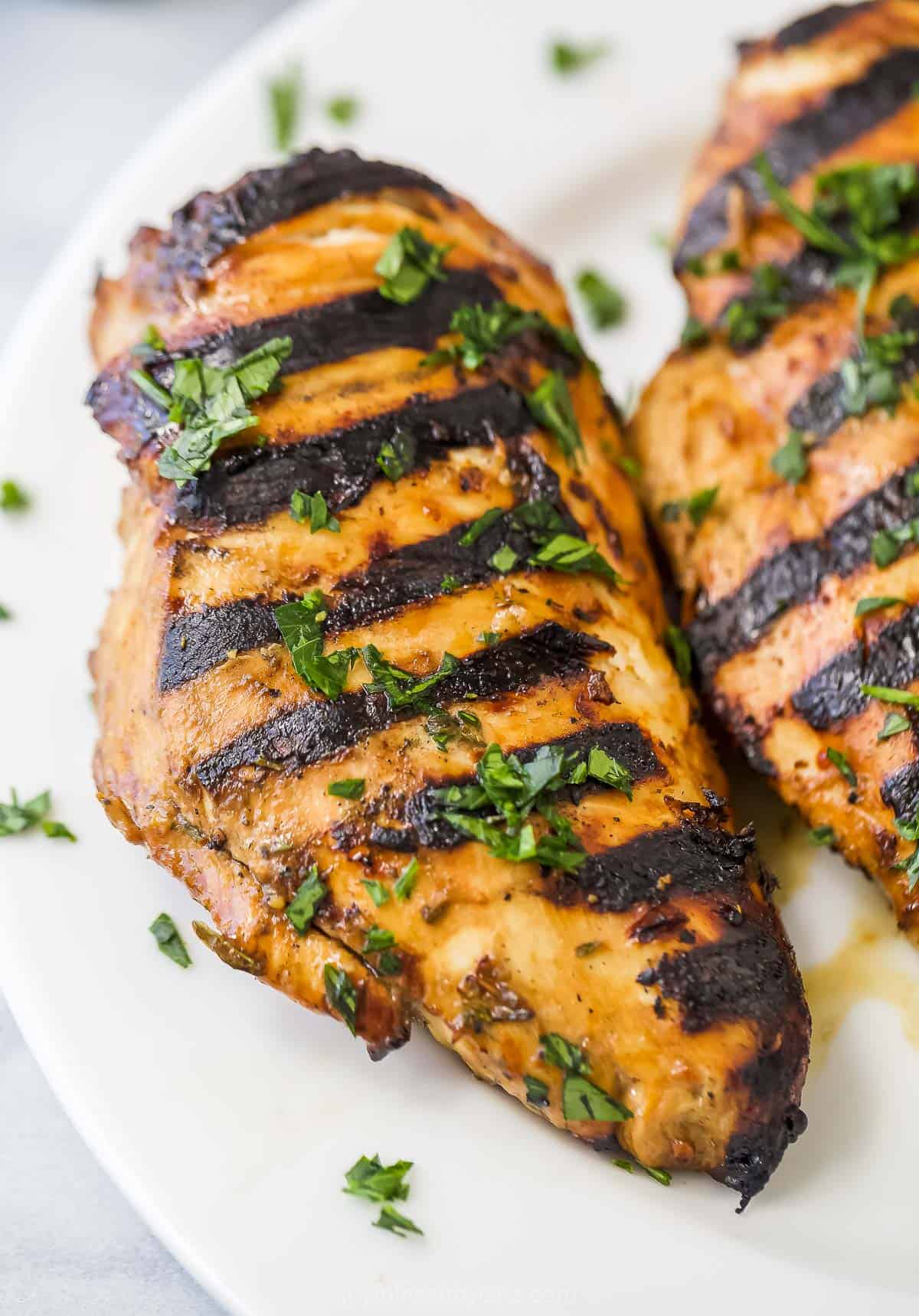 A marinated chicken breast with char marks on a plate beside a second breast