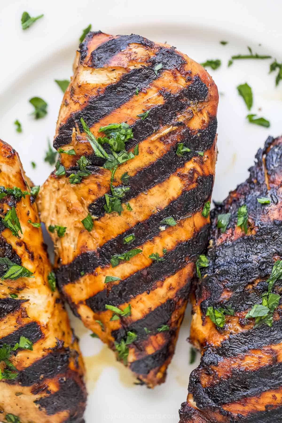 A close-up shot of a grilled chicken breast on a plate with another grilled chicken breast on either side of it