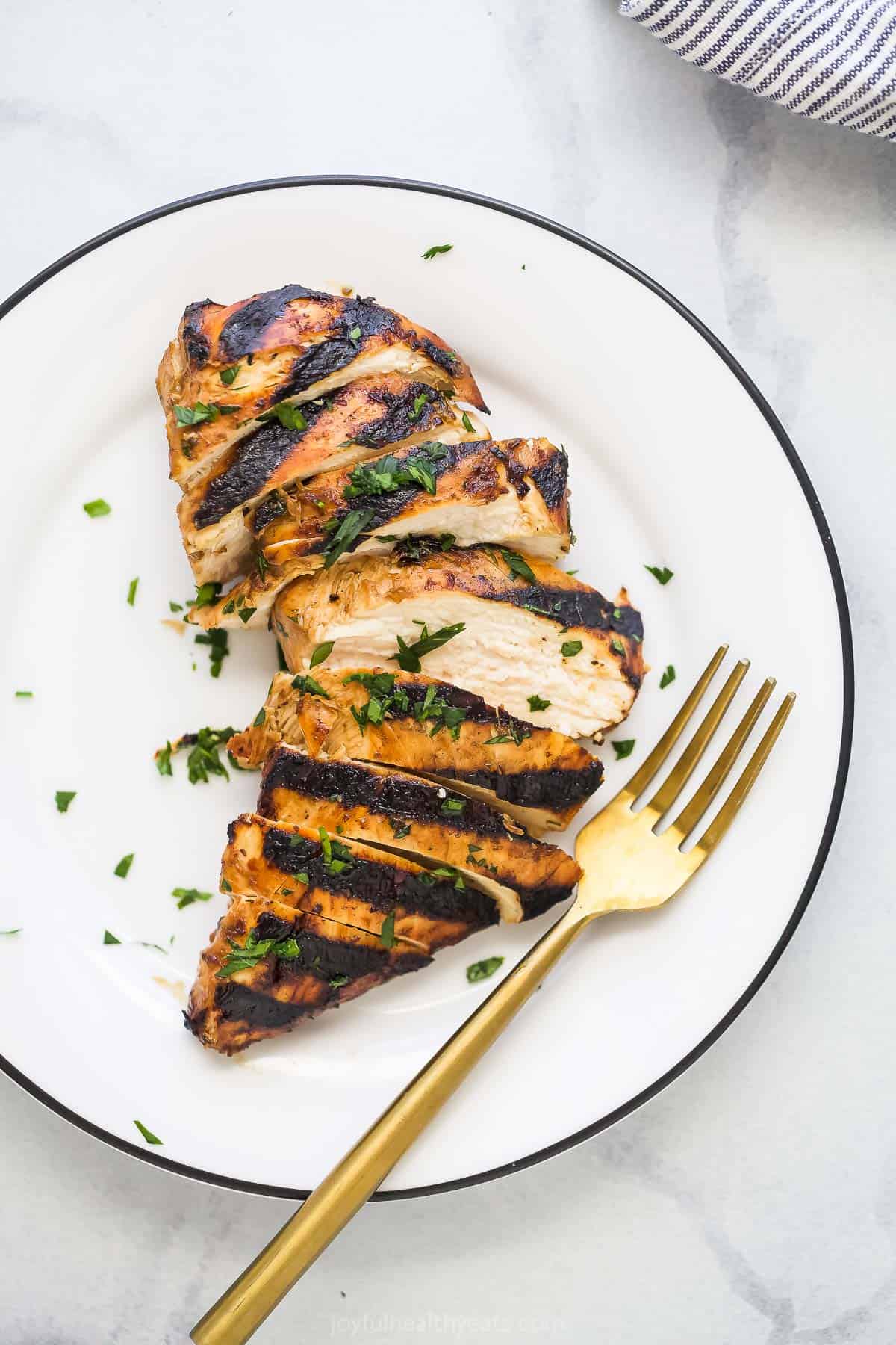 Pieces of balsamic grilled chicken on a platte with chopped parsley sprinkled on top