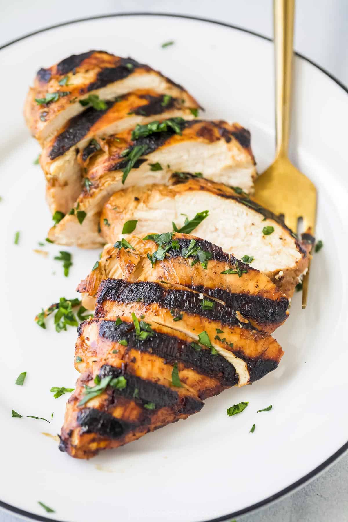 A grilled chicken breast cut into pieces on a plate with a golden fork
