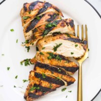 A grilled chicken breast sliced into eight pieces on a plate with chopped herbs on top