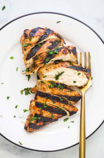 A grilled chicken breast sliced into eight pieces on a plate with chopped herbs on top