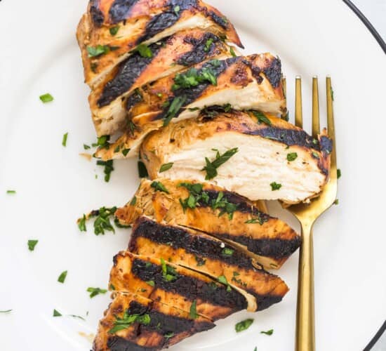 A grilled chicken breast sliced into eight pieces on a plate with chopped herbs on top