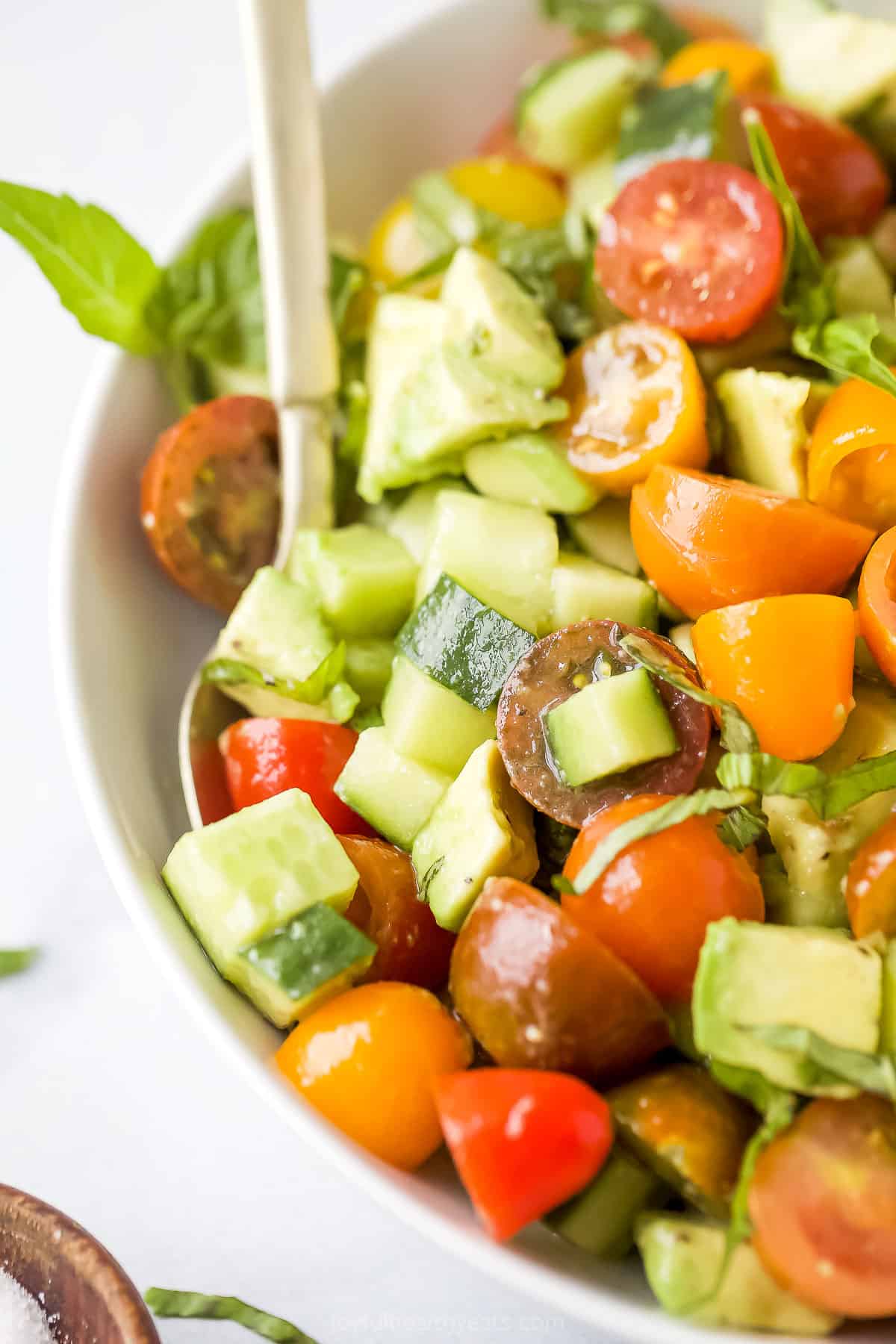 A close-up shot of an avocado tomato cucumber salad inside of a bowl with a spoon