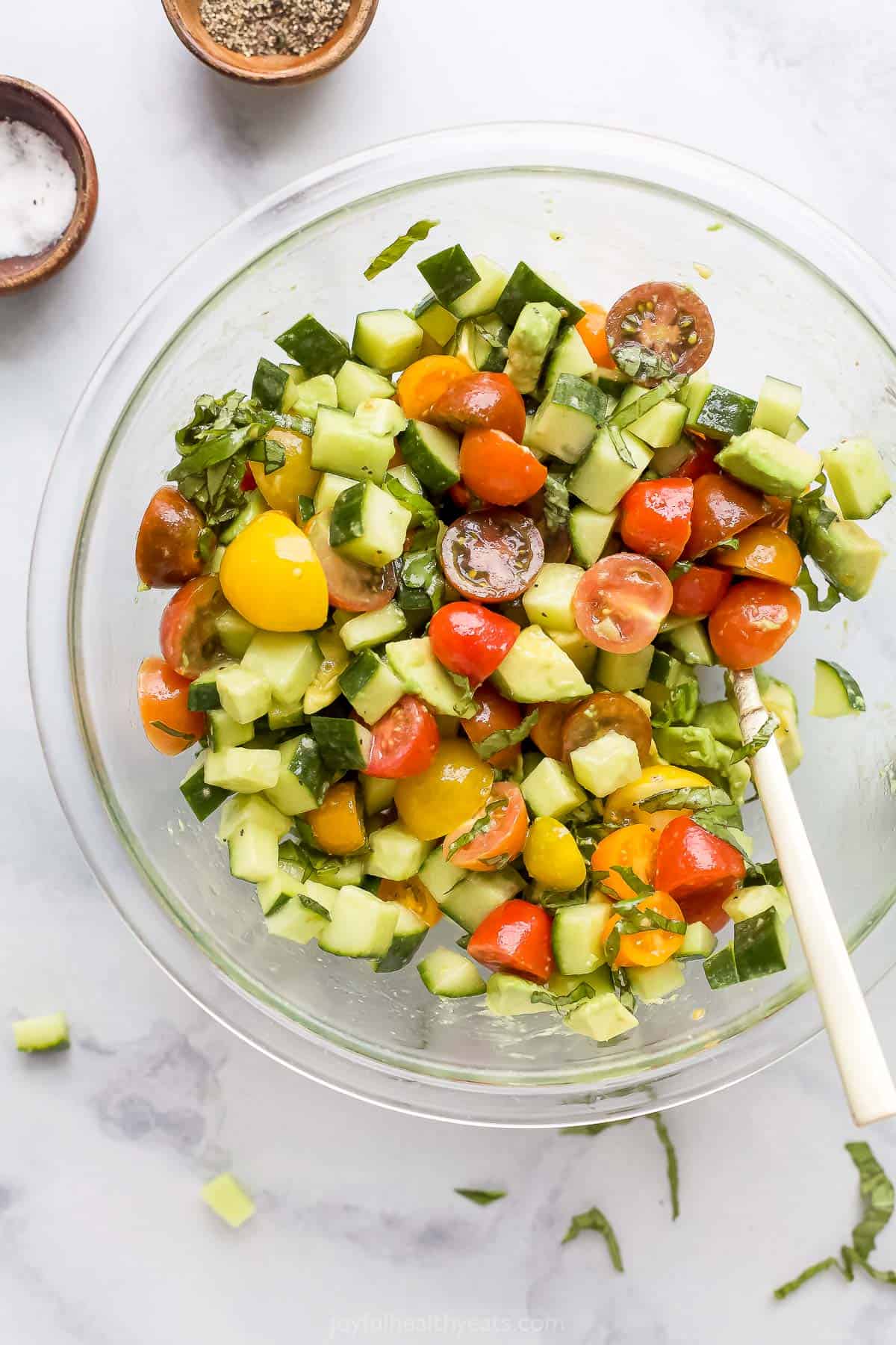 Chopped avocado, cucumber and tomatoes in a bowl with fresh basil and honey vinaigrette