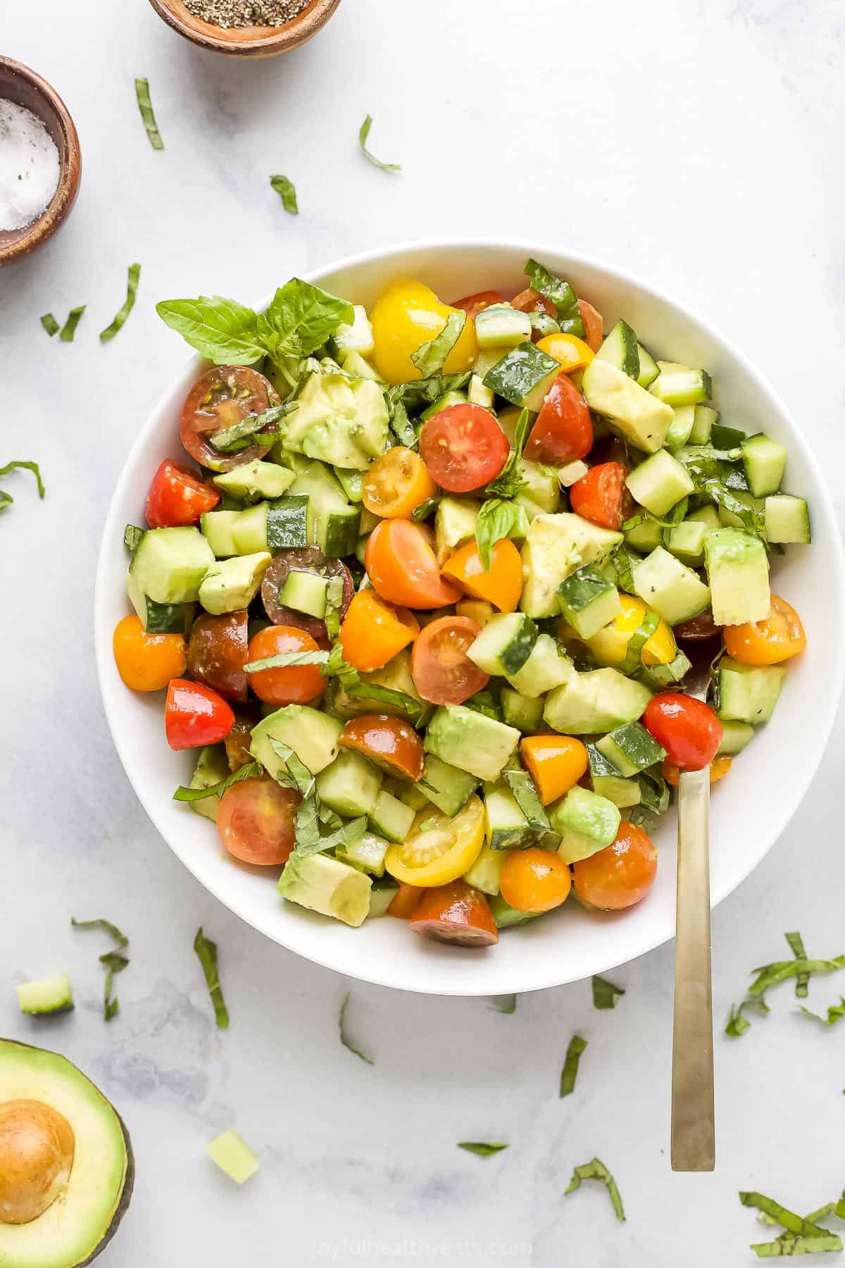 A bowl of avocado tomato cucumber salad with a basil leaf garnishing the dish