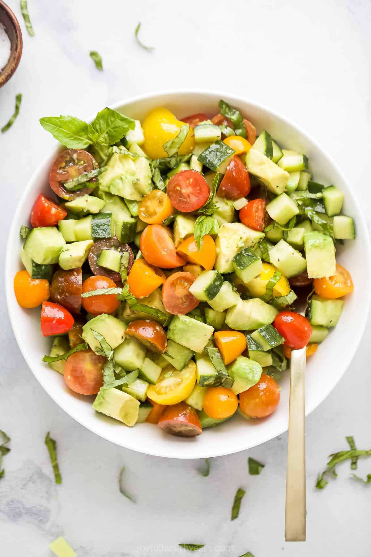 A bowl of salad on a marble countertop with chopped basil and a dish of salt