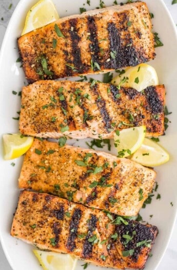 A long white serving platter holding four servings of grilled lemon pepper salmon