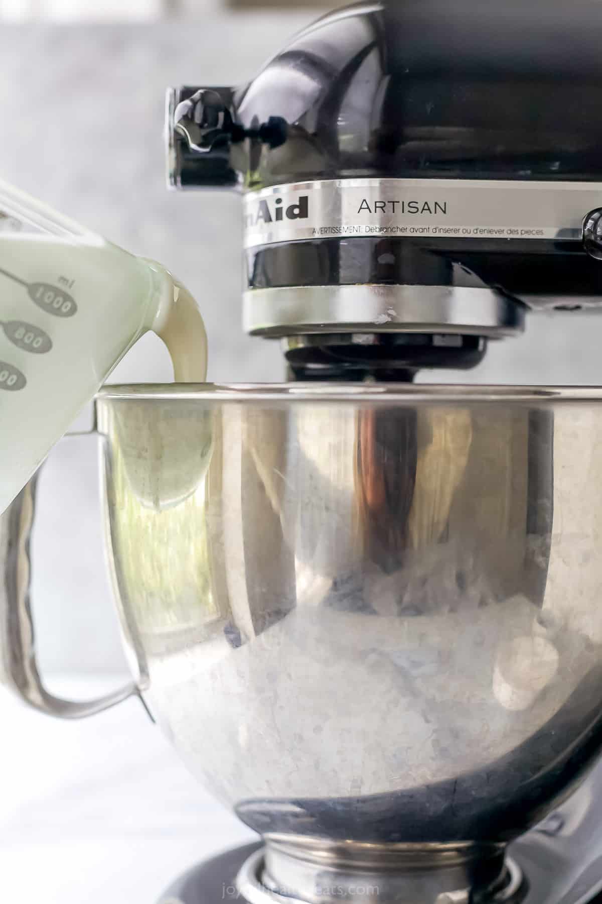 Heavy cream being poured into a metal mixing bowl