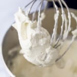 Homemade whipped cream inside of a bowl and on an electric whisk attachment