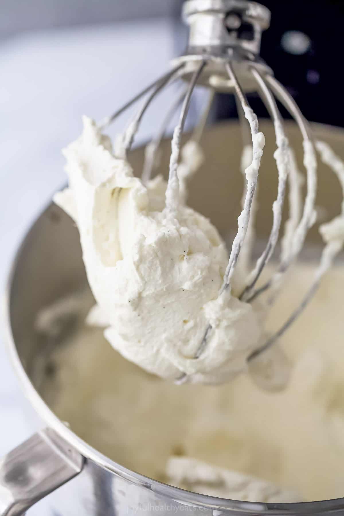 Homemade whipped cream inside of a bowl and on an electric whisk attachment