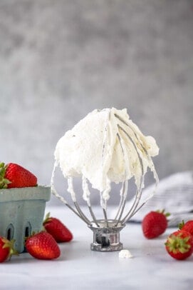 A stand mixer on a table with whipped cream all over it and fresh berries on either side of it