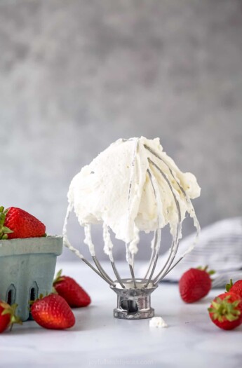 A stand mixer on a table with whipped cream all over it and fresh berries on either side of it