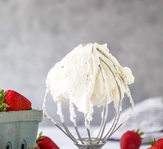 A stand mixer on a table with whipped cream all over it and fresh berries on either side of it