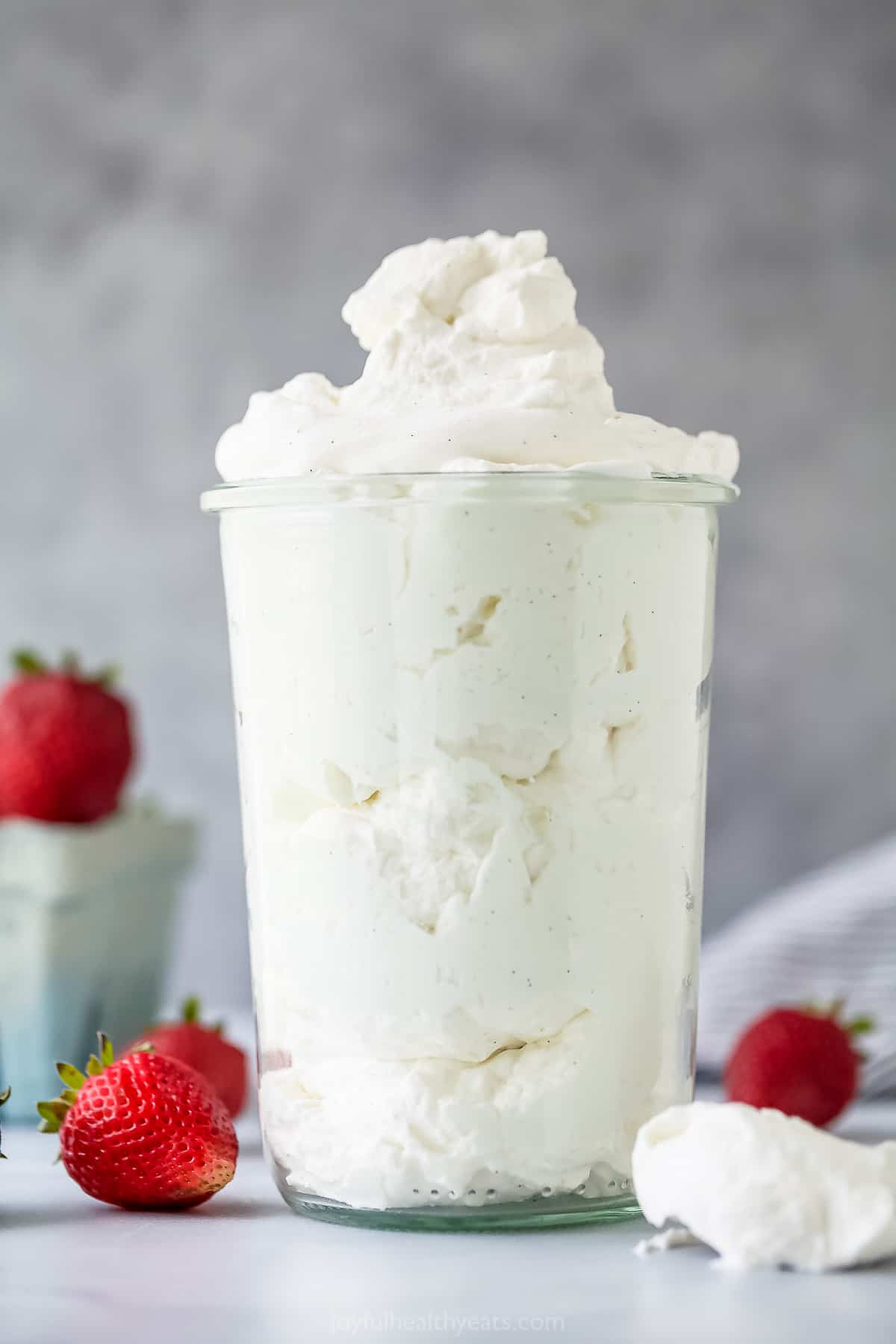 A large glass cup full of homemade whipped cream with fresh strawberries surrounding it