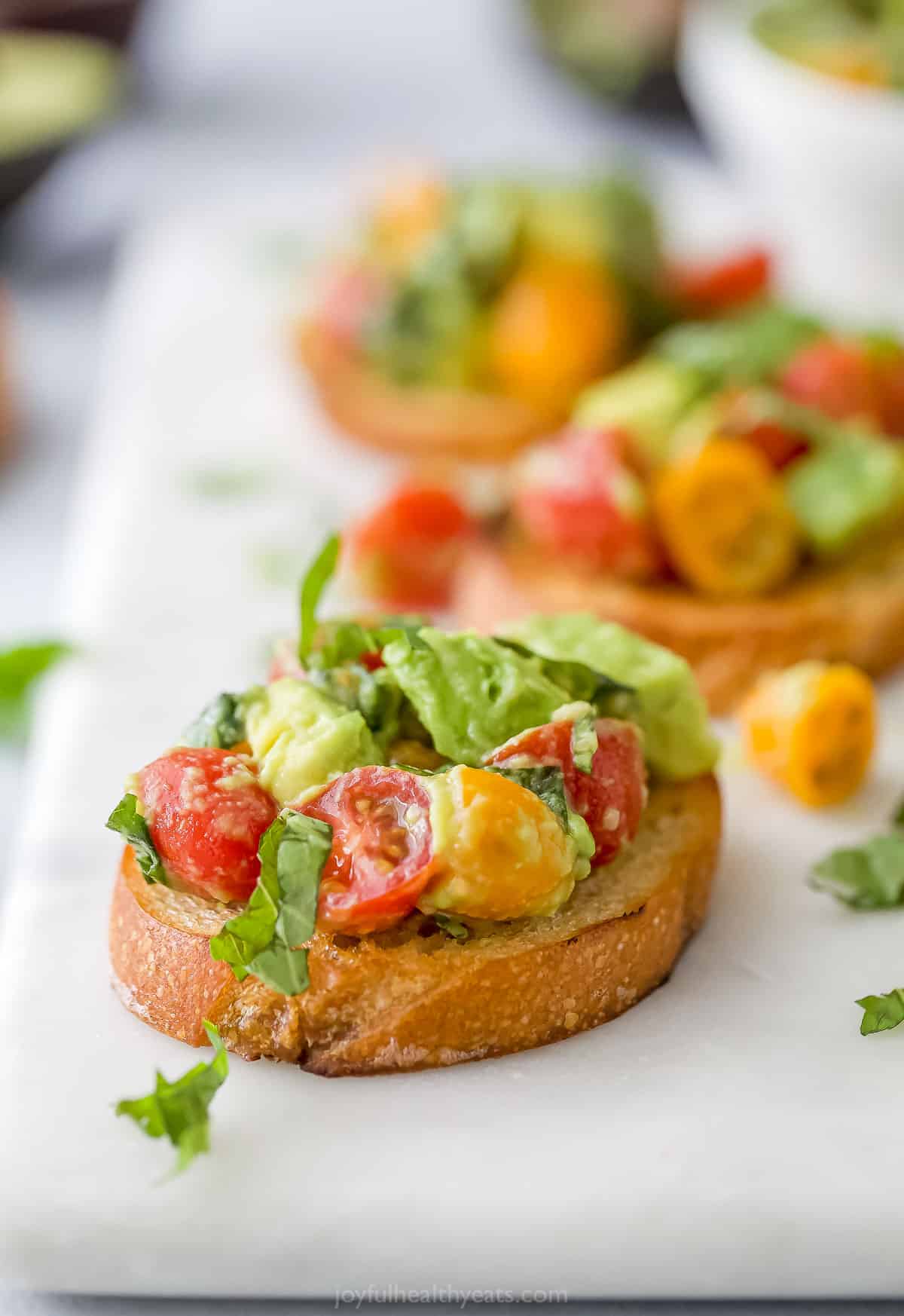 A piece of avocado bruschetta on a cutting board with two more slices behind it