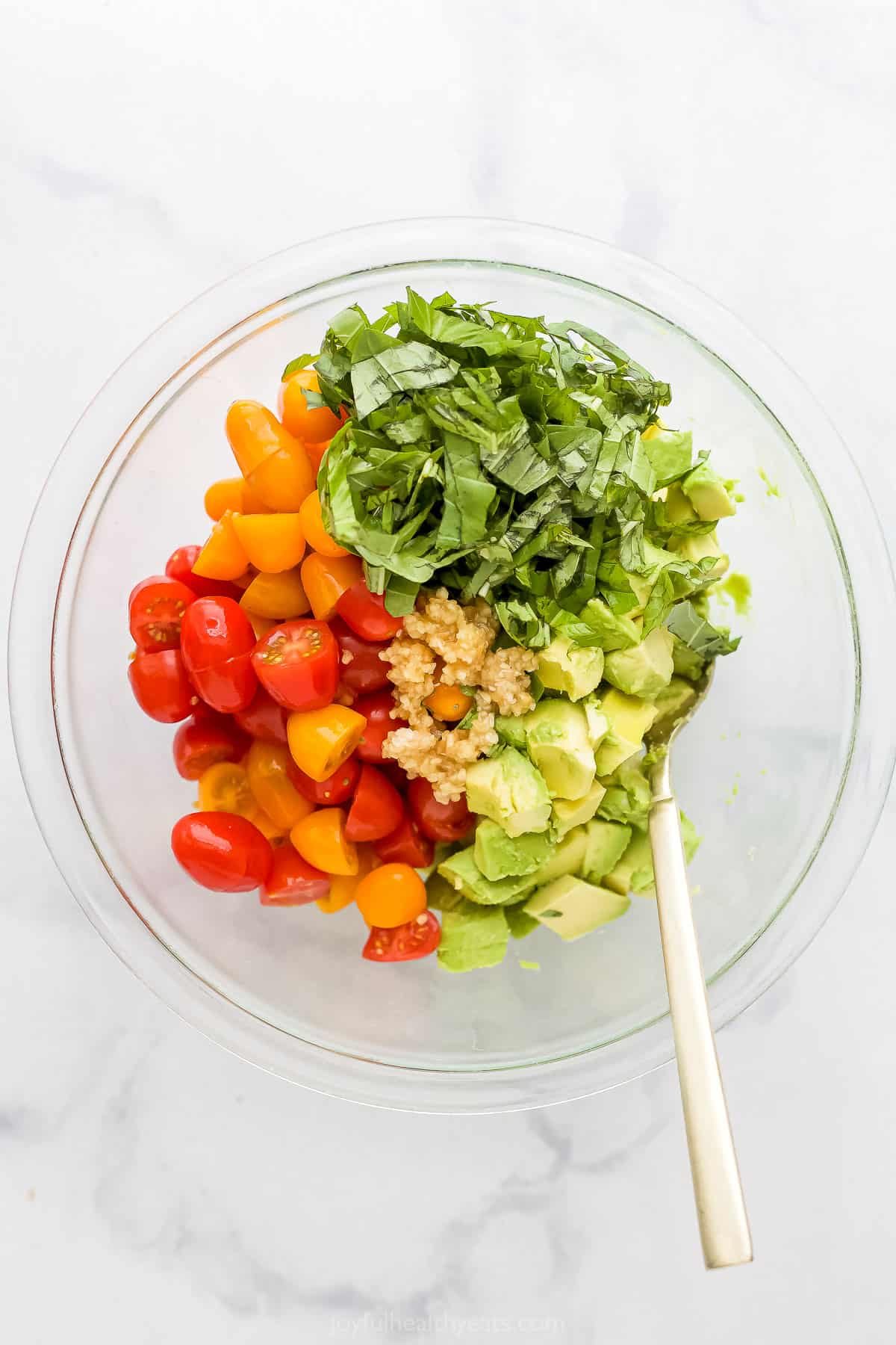 The prepared tomatoes, garlic, avocado and basil inside of a glass mixing bowl