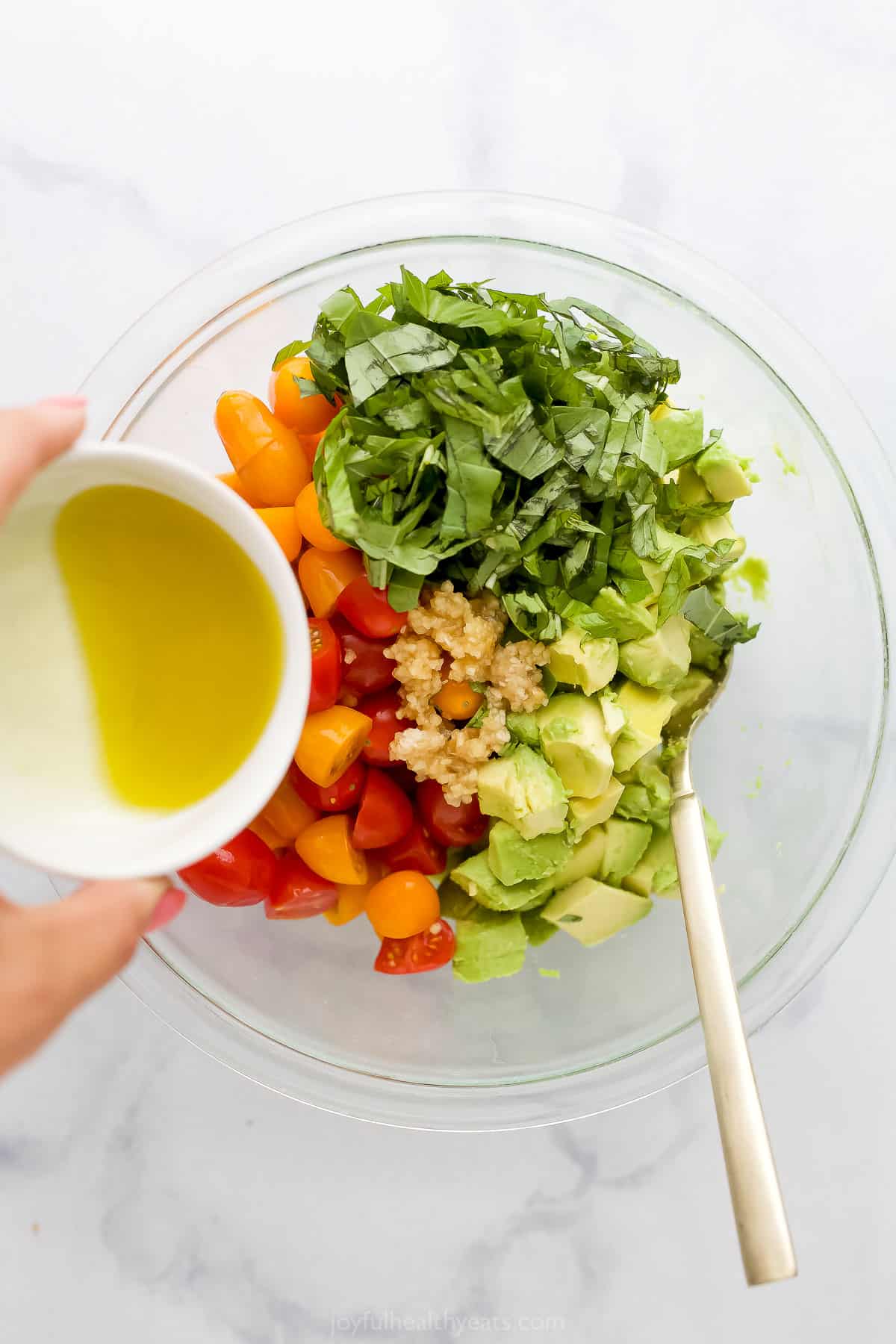 White balsamic vinegar being poured into a bowl full of minced garlic, fresh basil, chopped tomatoes and diced avocado