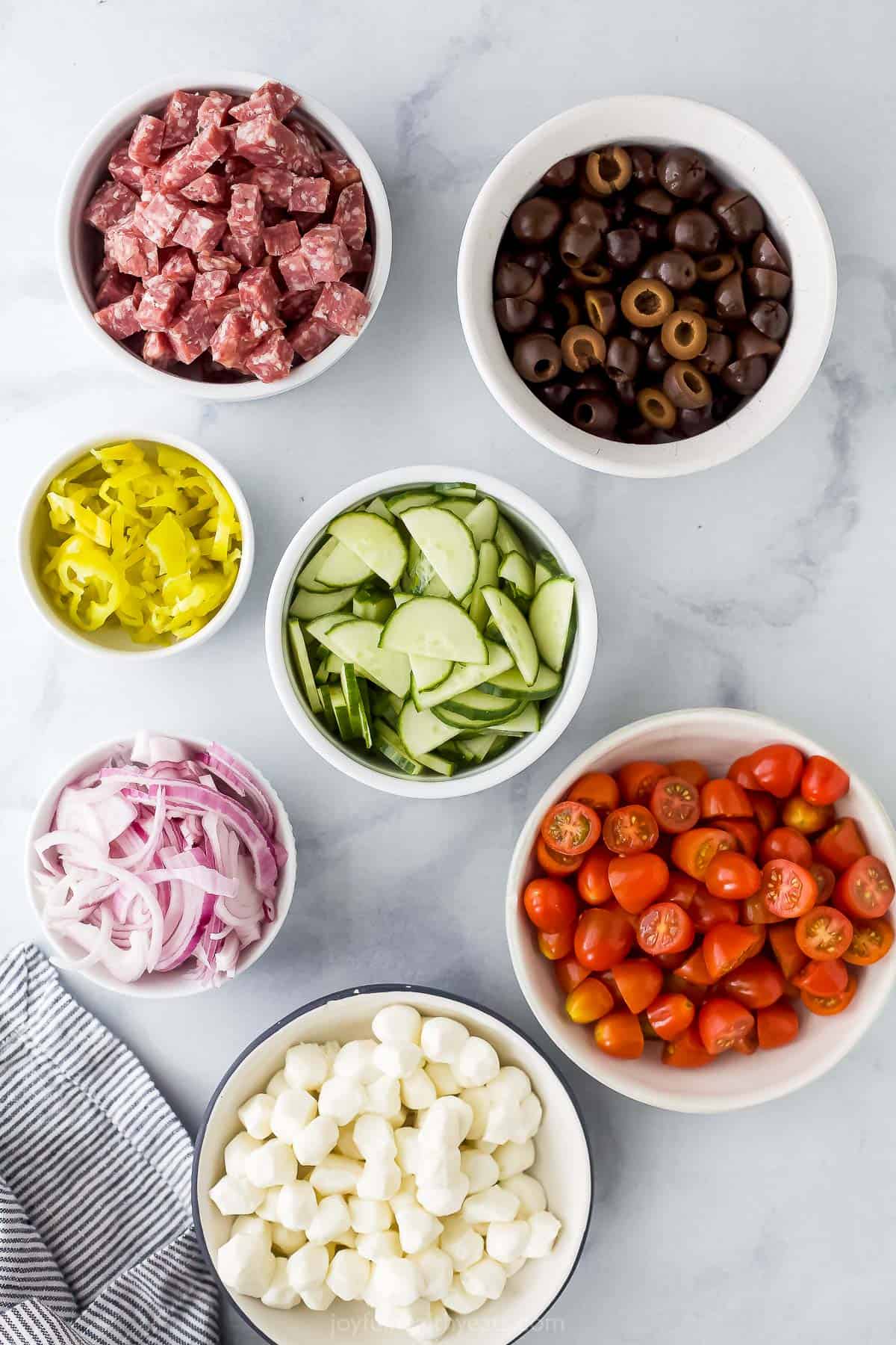 Mozzarella pearls, halved olives, chopped salami and the rest of the ingredients on a kitchen countertop