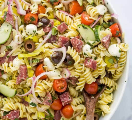 A large white serving bowl full of Italian pasta salad