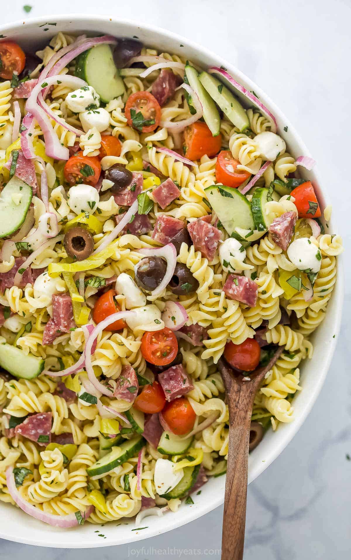 A large white serving bowl full of Italian pasta salad