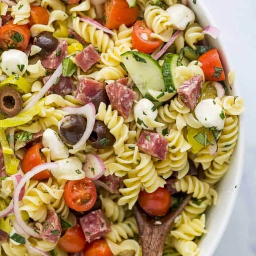 A close-up shot of a bowl of pasta salad with a wooden spoon inside