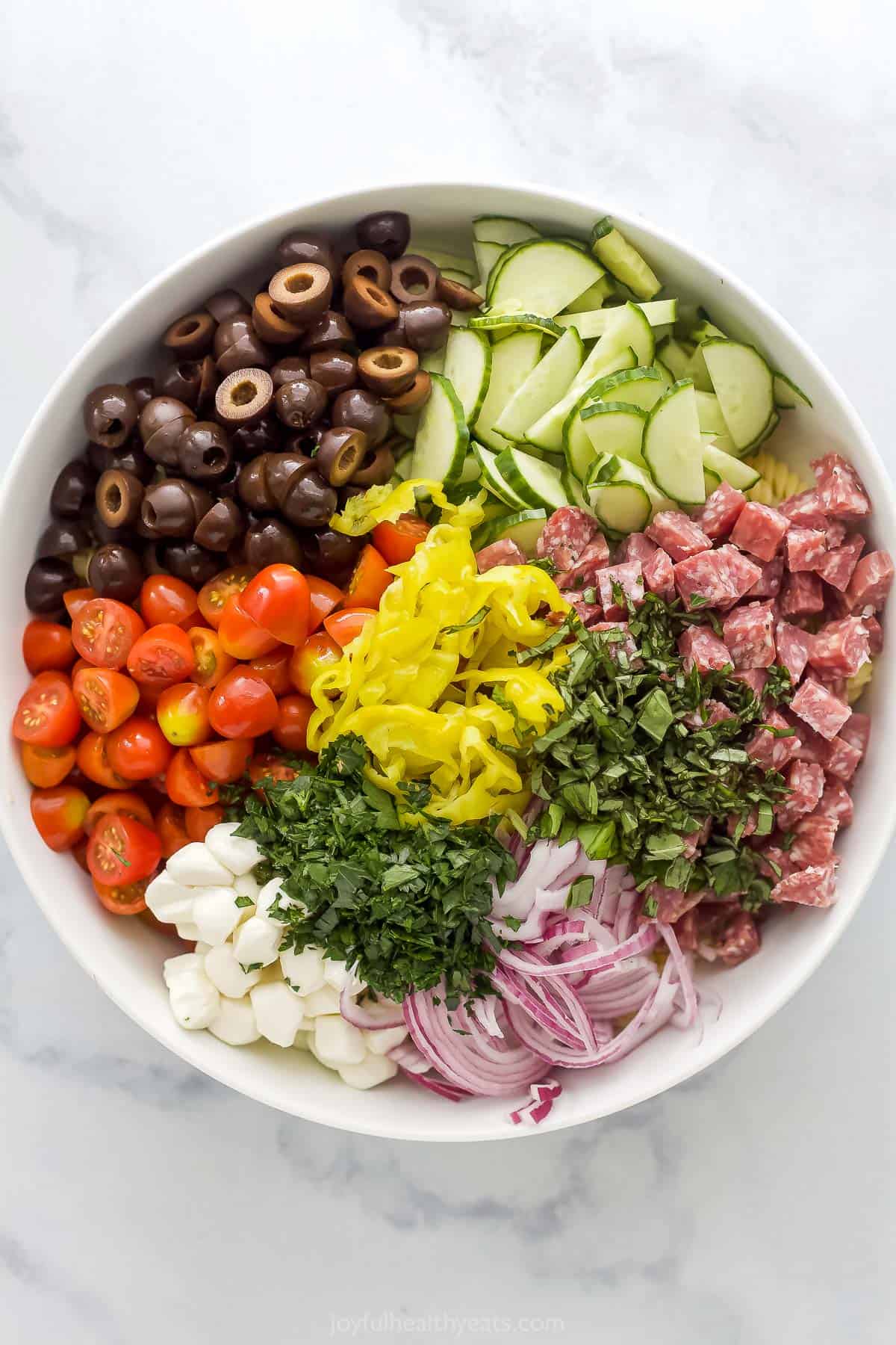 Various vegetables in a bowl with fresh herbs, mozzarella cheese, pasta and salami