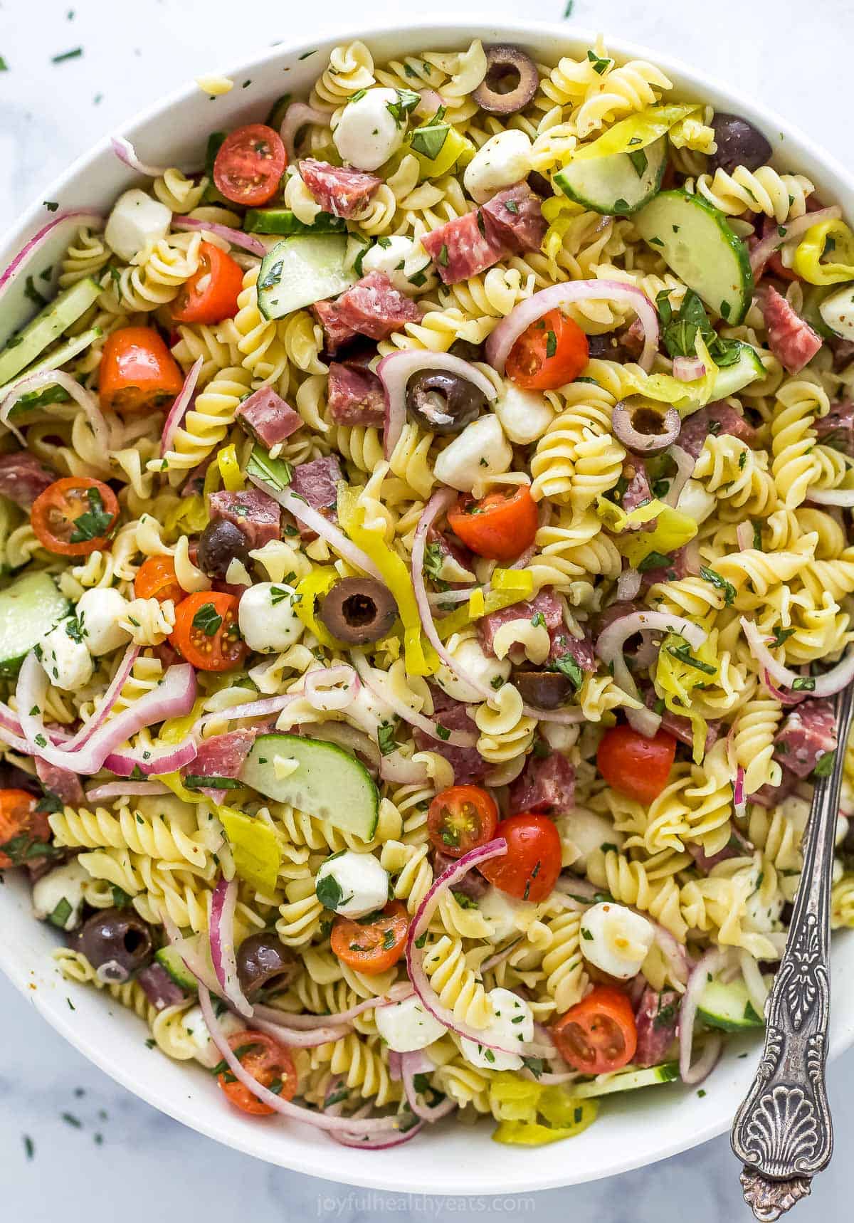 An overhead shot of pasta salad in a large bowl with a metal fork inside